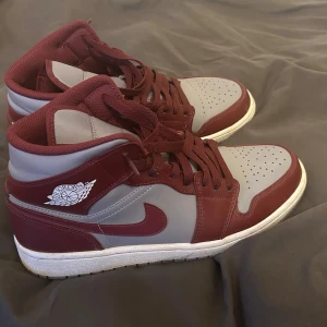Nike Air Jordan 1 vinröd/grå sneakers - Säljer ett par Nike Air Jordan 1 sneakers i vinrött och grått. Skorna är som ny skick, knappt använda. 26,5 cm strlk 42 och box finns kvar