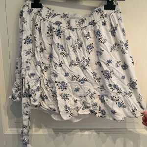 Vit blommig volangkjol från Hollister - Supersöt vit volangkjol från Hollister med blått blommönster och volangkant❤️Har även ett knyt band vid ena sidan och insydda shorts under(se bild 2) vilket är super praktiskt!!