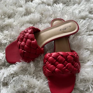 Röda flätade sandaler från Alley - Säljer ett par röda sandaler från Alley med bred, flätad rem över foten och fyrkantig tå. Snygg design med platt sula och mjukt material som ger en cool vibe till din outfit. Perfekt för dig som gillar att sticka ut med färg och detaljer.
