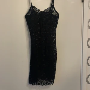 Svart spetsklänning med smala axelband - Supersnygg svart nästan genomskinlig kortklänning i spets med smala axelband och vågig kant nertill. Klänningen är figurnära och har en romantisk känsla med sitt genombrutna spetsmönster. Perfekt för dig som vill sticka ut. Helt ny har bara testat på!