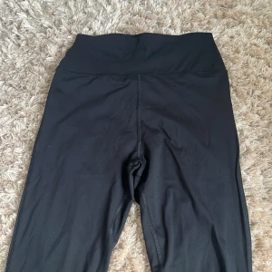 Svarta höga träningstights från ASOS 4505 - Nya svarta oanvända leggings från ASOS 4505 med hög midja och smidig passform. Tillverkade i stretchigt syntetmaterial som sitter tajt och bekvämt. Perfekta för träning eller chill. Snygg och enkel design som funkar till allt.