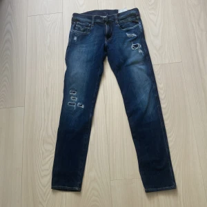 Replay Anbass blå jeans, storlek 28/30 - Säljer ett par Replay Anbass jeans i mörkblå tvätt med slitningar och snygga detaljer. Modellen är slim och har klassiska fem fickor, dragkedjegylf och broderade bakfickor. Perfekta för dig som gillar en modern och avslappnad look Ett litet märke på benet, se bild 5.