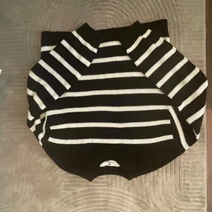 Svartvit randig stickad tröja - Snygg stickad tröja i svart och vitt med klassiskt randigt mönster. Tröjan har lång ärm och rund halsringning, perfekt för dig som gillar en stilren och tidlös look. Passar lika bra till jeans som till kjol är helt ny använd en gång 