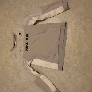 Nike Air grå sweatshirt Xs - Nike Air sweatshirt i grått med svarta loggor och text framtill. Tröjan har långärmade paneler i ljusgrått och vitt, rund halsringning och sportig look. Perfekt för dig som gillar streetwear och vill ha en clean stil.