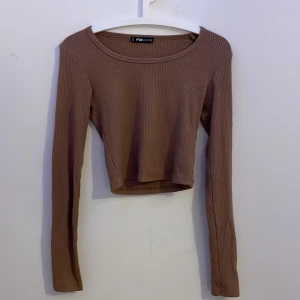 Ribbad croppad topp från FB Sister - Säljer en ribbad croppad långärmad topp från New Yorker i en snygg mörk beige nyans. Toppen har rund halsringning och är tillverkad i ett stretchigt material som sitter skönt på kroppen. Pris kan diskuteras!