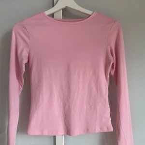 Ljusrosa långärmad topp - En enkel och stilren ljusrosa långärmad topp i mjuk bomull. Perfekt att matcha med jeans eller kjol för en clean look. Rund halsringning och rak passform gör den både bekväm och lätt att bära.