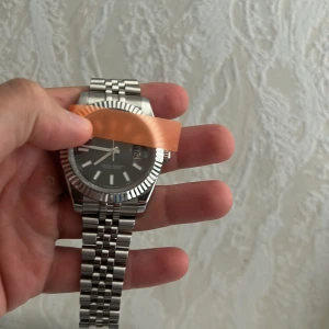 Datejust silverfärgad klocka - Säljer en stilren Datejust med silverfärgad länk i rostfritt stål och mörk urtavla. Klockan har räfflad bezel, datumvisning och klassisk jubilee-länk. Extra länkbitar medföljer. Perfekt för dig som gillar exklusiva accessoarer. Automatisk med extra länkar