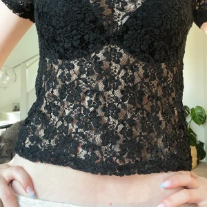 Svart spetstopp - Supersnygg svart topp i spets med blommigt mönster. Kortärmad och figurnära passform, perfekt att styla över ett linne eller under T-shirt!! Vet inte vart den är ifrån då lapparna är bortklippta💓