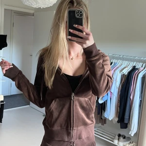 Brun velour hoodie med dragkedja - Mysig brun hoodie i velour med huva och dragkedja framtill. Jackan har ribbade muddar, fickor på magen och en avslappnad passform. Perfekt för en chill och trendig look. + Byxor