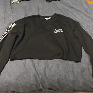 Svart croppad sweatshirt med tryck - Svart croppad sweatshirt med texten 'THE BEST VERSION' på bröstet och vita tryck längs båda ärmarna. Tröjan har rund halsringning och långa ärmar. Perfekt för en chill och trendig look.