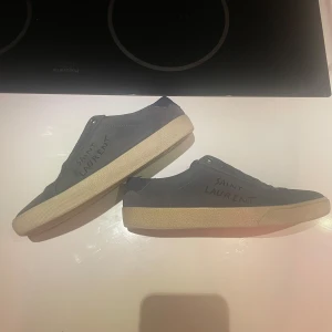 Saint Laurent ljus blå mocka skor - Pris nya: 7100kr. Det är strl 38 men passar 39. Snygga sneakers från Saint Laurent i ljus blå mocka med handskriven logga på sidan. Original snören medföljer. Skorna har vit platt sula och mörkblå detaljer. Tillverkade i Italien 🇮🇹 och är stilrena. De passar till det mesta. 