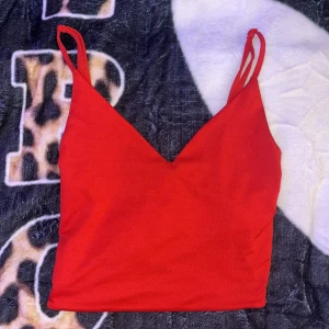 Röd croppad linnetopp med smala band - Snygg röd croppad linnetopp med smala axelband och v-ringad halsringning. Toppen har enkel design och justerbara band för perfekt passform. Perfekt för att styla med jeans eller kjol när du vill sticka ut lite extra.