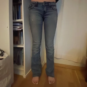 True Religion bootcut jeans blå, stl 24 - Säljer ett par blå bootcut jeans från True Religion med ikoniska bakfickor och markerade sömmar. Jeansen har låg midja, slitningar och hål vid knät. Storleken är 24 och passar mig som är 166cm lång och brukar ha xs i byxor.