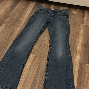 Blå bootcut jeans från Gina Tricot - Snygga blå jeans från Gina Tricot i modell med bootcut. Klassisk femficksdesign, orangea kontrastsömmar och knappdetaljer. Jeansen har en normal passform och är tillverkade i slitstarkt denimtyg. Perfekta för dig som gillar en tidlös look.