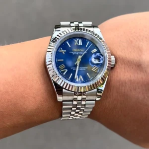 Seiko Datejust blå urtavla herrklocka - Stilren Seiko Datejust herrklocka med blå urtavla, romerska siffror och datumfönster. Klockan har en klassisk rund form, räfflad silverfärgad bezel och länkarmband i blankt stål. Perfekt accessoar för dig som gillar tidlös design.