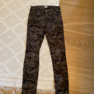 Camo jeans från ONLY - Snygga camouflage-mönstrade skinny jeans från ONLY. Byxorna har klassisk femficksdesign, gylf med dragkedja och knapp, samt låg midja. Färgerna går i grönt, brunt och svart. Perfekta för dig som vill sticka ut med en cool streetstyle.