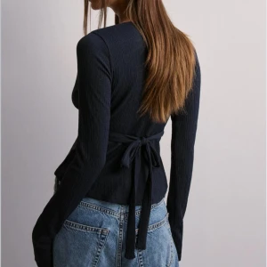 Marinblå omlottopp med v-ringning - Supersnygg marinblå omlottopp från nelly med en snygg v-ringning och långa ärmar. Toppen har knytband i midjan. Säljer då den inte används💕Den finns ej i storlek på hemsidan!