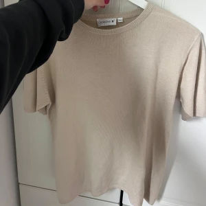 Beige stickad kortärmad tröja Georgina B. - En stilren beige stickad tröja från Georgina B. med korta ärmar och rund halsringning. Tröjan har en enkel och clean look, perfekt för dig som gillar minimalistisk stil. Mjuk och skön kvalitet som passar året runt.