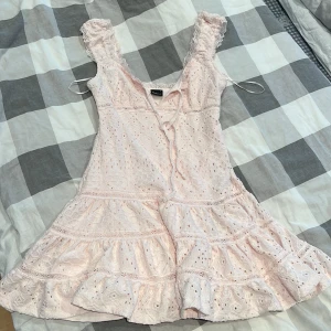 Ljusrosa spetsklänning Gina Tricot S - Supersöt ljusrosa kortklänning från Gina Tricot med volanger, spetsdetaljer och knyt framtill. Klänningen har ärmlös design med breda axelband och romantiskt mönster. Perfekt för sommarens alla tillfällen!