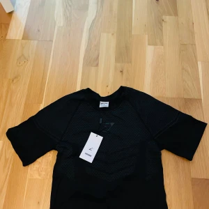 Svart Gymshark t-shirt i mesh - Svart t-shirt från Gymshark med diskret mönster och sportig meshstruktur. Perfekt för träning, med korta ärmar och lätt material som andas. Snygg och funktionell för dig som gillar att hålla stilen på gymmet. ⚠️Denna vara är ej autentisk⚠️