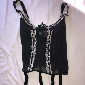 Svart spetskorsett med vita detaljer - Säljer en svart korsett med transparent mesh och vita spetsdetaljer längs kanterna. 