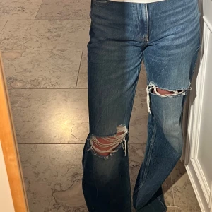 Blå ripped wide jeans från Zara - Säljer ett par blå jeans från Zara i modell med breda ben och snygga slitningar över knäna. Jeansen har hög midja, klassiska fem fickor och är tillverkade i bomull. Perfekta för en avslappnad och trendig look.