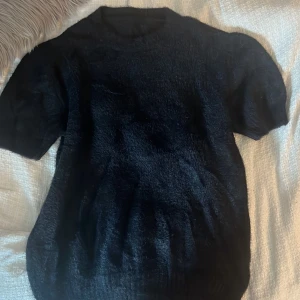 Svart fluffig t-shirt - Mysig svart t-shirt med korta ärmar och rund hals. Tröjan är fluffig och stickad! Den är ifrån vinted och saknar lapp men passar främst S/M tror jag💕💕 Knappt använd, bra skick!
