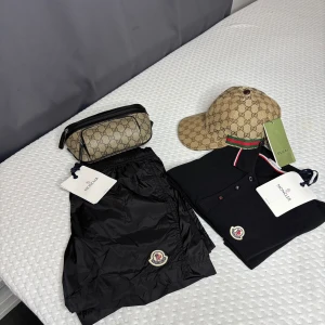 Svarta Moncler shorts med snörning - Svarta shorts från Moncler i glansig syntet med elastisk midja och snörning. Klassisk Moncler-logga framtill och bakficka med dragkedja och röd-vit-blå detalj. Perfekta för sommaren och chill dagar.