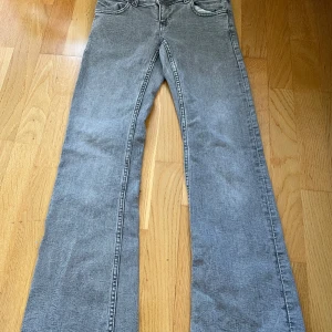 Grå bootcut jeans Gina Tricot stl 152 - Grå jeans från Gina Tricot i bootcut-modell med cool vit stjärna på bakfickan. Jeansen har klassisk femficksdesign, knappgylf och är tillverkade i mjukt denimtyg. Perfekta för dig som gillar en avslappnad men trendig look.
