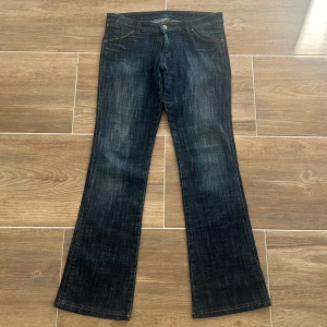 Lågmidjade utsvängda jeans  - Ett par lågmidjade utsvängda jeans från Wrangler i storlek W31 L34. Rakt över midjemått: 41cm. Innebenslängd: 75cm. Total längd: 98cm. Gren: 21cm. Benslut: 21cm. D31