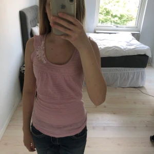 Rosa linnetopp med spetsdetalj - Supersöt ljusrosa linnetopp från Soyaconcept med broderad spetsblomma vid ena axeln. Tunt, mjukt material med diskret struktur och rundad halsringning. Perfekt för varma dagar när du vill ha något både gulligt och bekvämt. Storlek XS!