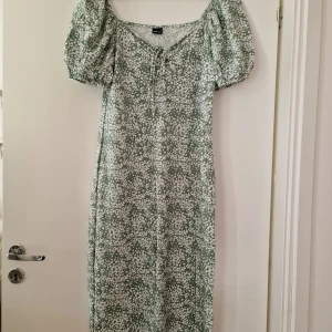 Grön blommig klänning från Gina Tricot - * Först bild är inte min bild, bara ville visa hur klänningen ser ut när den bärs*Supersöt grön långklänning med vitt blommönster från Gina Tricot. Klänningen har puffärmar, v-ringning med snörning och en snygg slits framtill. Perfekt för sommarens alla tillfällen och ger en romantisk vibe. Storlek L, använd få gånger.