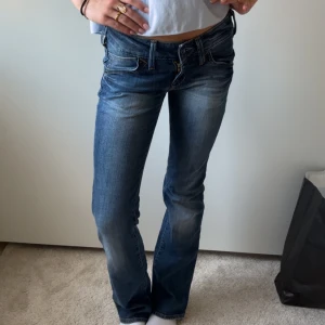 Blå bootcut jeans från Lee - Säljer ett par snygga blå jeans från Lee med klassisk bootcut-modell. Jeansen har låg midja, lätt slitningar framtill och bakfickor med dekorativa sömmar. Perfekta för dig som gillar en avslappnad men ändå trendig look.