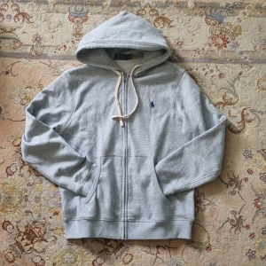 Grå zip- hoodie från Polo Ralph Lauren - Tjena! Säljer denna asfeta zip-hoodien från Polo Ralph Lauren. Tröjan är i en stilren ljusgrå färg med den klassiska broderade loggan på bröstet. Den har också en huva med snörning, dragkedja framtill och kän. Tillverkad i mjuk bomullsmix, perfekt för chill dagar eller när du vill ha en clean look. Kontakta gärna vid eventuella frågor 👊 Obs; pris kan diskuteras vid snabb affär!