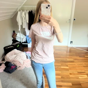 Ljusrosa Nike t-shirt med logga - Säljer en ljusrosa t-shirt från Nike i bomull med klassisk vit Nike-logga framtill. T-shirten har rund halsringning och korta ärmar. Storlek XS.