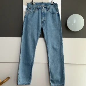 Levi's 501 ljusblå jeans straight fit - Klassiska Levi's 501 jeans i ljusblå denim med rak passform och hög midja. Jeansen har fem fickor, knappgylf och den ikoniska röda Levi's-taggen på bakfickan. Perfekta för en avslappnad och tidlös stil. Använt en gång. 