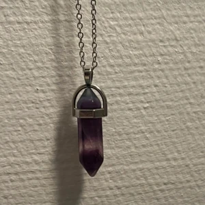 Halsband med lila kristallhänge - Snyggt halsband med en silverfärgad kedja och ett spetsigt lila kristallhänge. Hänget har en cool geometrisk form och sitter fast i ett metallfäste. Perfekt för dig som gillar kristaller och vill ha en unik detalj till din stil.