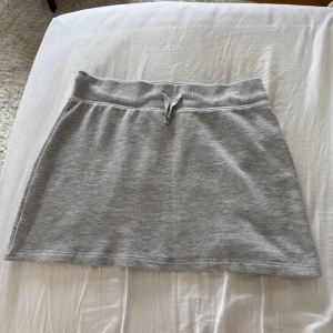 Grå kortkjol från BikBok med snörning - Enkel och snygg grå kortkjol från BikBok i mjukt bomullsmaterial. Kjolen har bred resår i midjan och en liten snörning framtill för extra detalj. Perfekt för en chill och avslappnad stil. Endast använd ett fåtal gånger, så den är i nyskick ! 🥰pm för fler bilder !😊