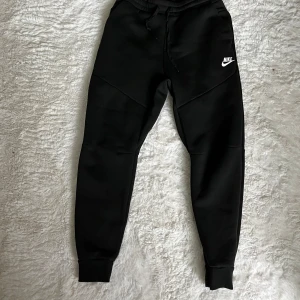 Svarta mjukisbyxor från Picken - Svarta mjukisbyxor från Picken med dragsko i midjan och ribbade muddar vid bensluten. Byxorna har en klassisk, avslappnad passform och är tillverkade i mjukt material som känns skönt mot huden. Perfekta för chill eller träning.