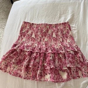 Blommig volangkjol från Gina Tricot - Supersöt kort kjol från Gina Tricot med rosa och vita blommor. Kjolen har smockad midja och dubbla volanger nertill som ger en flowy känsla. Perfekt för dig som gillar romantisk och feminin stil. Använd flitigt , men i super skick. Inga tecken på användning 🥰Pm för fler bilder !💓