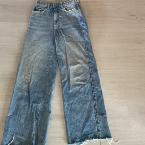Blå wide jeans från Gina  - Snygga blå jeans från Gina i modell med raka, vida ben och råa, fransiga benslut. Klassisk femficksdesign och hög midja. Perfekta för en avslappnad och trendig look.