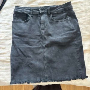 Svart jeanskjol från Pieces XS - Svart jeanskjol från Pieces i klassisk femficksmodell. Kjolen är kort och har rå, fransig kant nertill för en cool vibe. Gjord i stretchig denim med bälteshällor och dragkedja framtill. Perfekt till sneakers eller boots.