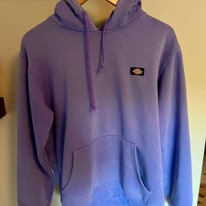 Lila hoodie från Dickies med huva - Säljer en lila hoodie från Dickies i storlek medium. Tröjan har huva med snörning, magficka och Dickies-logga på bröstet. Perfekt för dig som gillar streetwear och vill ha en chill look. Materialet är mjukt och skönt, troligtvis bomull eller polyester.