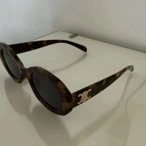 Bruna Céline solglasögon oval form - Snygga solglasögon Céline inspirerade med oval form och sköldpaddsmönstrade bågar i bruna och svarta toner. Guldigt logodetalj på sidorna ger en lyxig touch. 