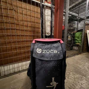 Svart Züca resväska med rosa handtag - Cool svart resväska från Züca med rosa handtag och silvriga detaljer. Väskan har ett tryck med konståkningsmotiv och små glittriga prickar framtill. Perfekt för att rulla med sig till träning eller tävling. Snygg och praktisk design med flera fack.