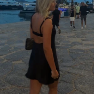 Svart kort satinklänning med smala axelband - Supersnygg svart mini klänning i satin med smala, rynkade axelband och öppen rygg. Figurnära passform upptill och lätt utsvängd nertill. Tjej på första bilden är 161 och på sista 168. Passar en S eller M med mindre bröst 