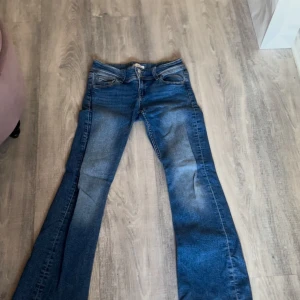Blå bootcut jeans Gina Tricot 152 - Snygga blå bootcut jeans från Gina Tricot i storlek 152. Jeansen har klassisk femficksdesign, markerade sömmar och tre knappar i midjan. Materialet är jeans med en skön stretch och tvättade detaljer för en cool look.