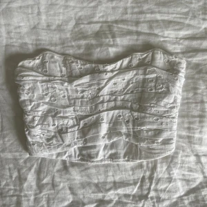 Vit broderad tubtopp från Zara - Säljer en söt vit tubtopp med broderade detaljer och små hålmönster. Toppen har en smockad baksida för extra komfort och sitter snyggt på kroppen. Perfekt för varma dagar och somriga outfits!