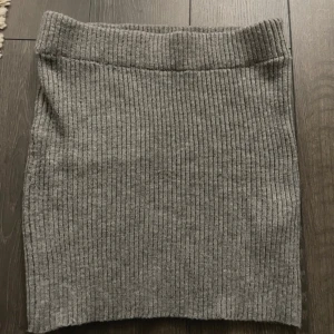 Grå ribbad kjol - Säljer en enkel och stilren grå ribbad kjol i stickat material. Kjolen är rak i modellen och har en bekväm midjeresår. Perfekt att matcha med en oversized tröja eller en snygg topp.