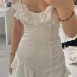 Vit volangklänning med axelband - Har aldrig använt. Perfekt för studenten,  alla tillfällen! Materialet känns lätt och svalt.